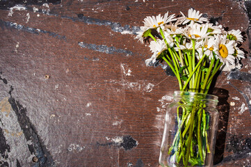 Bouquet of daisies in a glass jar on a wooden background. Symbol of purity and freshness, skin cosmetics