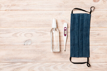 Top view of homemade cotton mask, digital thermometer and alcohol hand sanitizer on wooden background. Health care concept with copy space