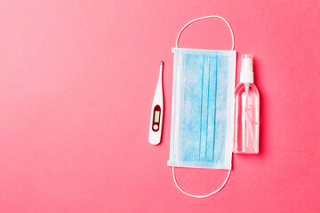 Fototapeta na wymiar Top view of surgical mask, digital thermometer and alcohol hand sanitizer on pink background. Health care concept with copy space