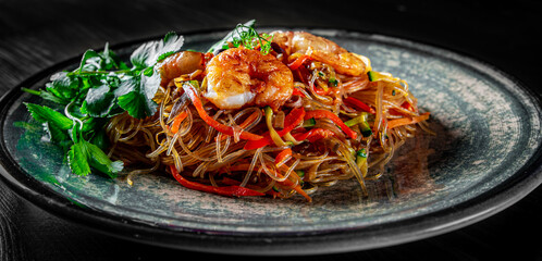 Stir fry noodles with vegetables and shrimps in plate on wooden table background