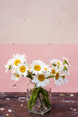 Bouquet of daisies in a glass jar on a wooden surface on a pink background