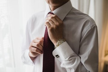 man tightens his tie, groom in a white shirt, wedding day