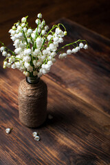 Delicate bouquet of lily of the valley in a vintage vase on a wooden table. Selective focus.