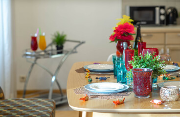 Close-up of set table in modern interior of kitchen in studio apartment. Empty clean dishes and glasses. Green flowers.