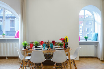 Modern interior of spacious studio apartment. Set table. Cozy sofa. Clean dishes. Big arch windows. Pillows on the sills.