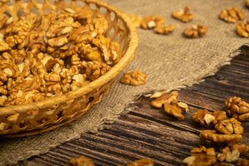 Peeled walnuts in a wicker basket and peeled walnuts scattered on a wooden table covered with rough-textured burlap. Healthy diet. Fitness diet. Close up.