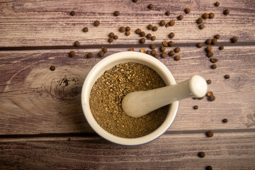 Allspice in a ceramic mortar and scattered allspice on a wooden table. Close up.