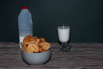 Homemade sugar cookies in a bowl on the table. Behind are a glass of milk and a bottle half filled with milk.
