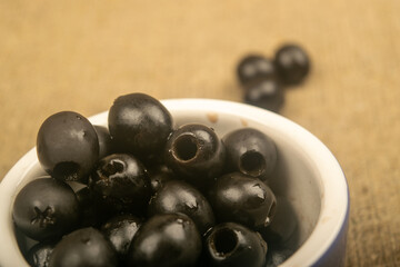 Black seedless olives in a ceramic bowl and a few scattered olives on a background of...