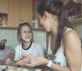 Daughter and mother sit in the kitchen at the table and cook from the dough. A woman teaches a girl to cook deliciously. They have fun and joyful time with each other. High quality photo