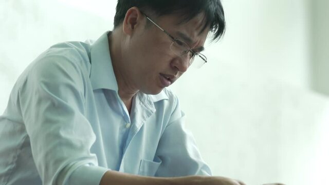 4K Stressed Asian businessman sitting in the house with reading financial bill and think of debt problem. Entrepreneur man worry about money management. Mental health and economic problem concept