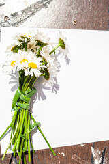 White blank sheet and a bouquet of daisies on a wooden background. The concept of cleanliness, perfume, skin care