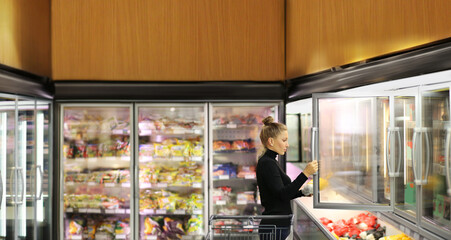 Woman choosing frozen food from a supermarket freezer. purchasing a packet of meat at the...