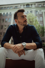 Young man sits and ponders on bench near building.