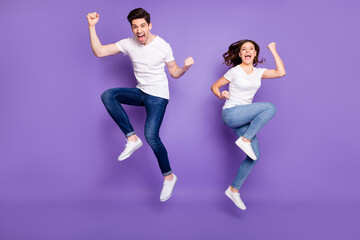 Full length photo pretty lady handsome guy couple jumping high up raise fists sporty competitions supporters fans wear casual t-shirts jeans pants shoes isolated purple color background