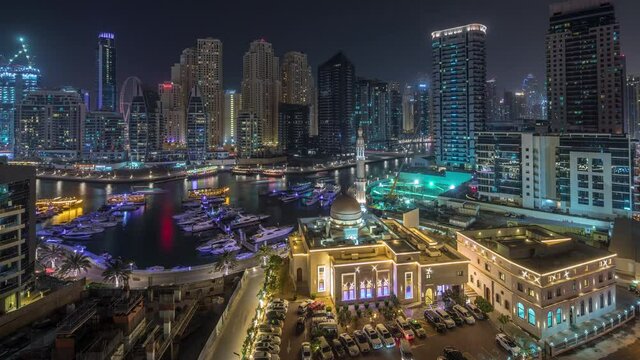 Yachts in Dubai Marina flanked by the Al Rahim Mosque and residential towers and skyscrapers aerial day to night transition timelapse. Modern high rise skyline with boats and wooden dhows