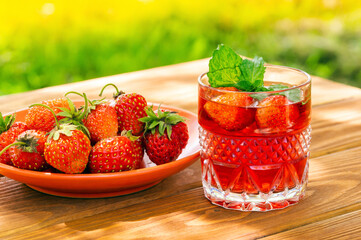 Strawberries in plate on the table and fresh drinks with mint on a sunny day