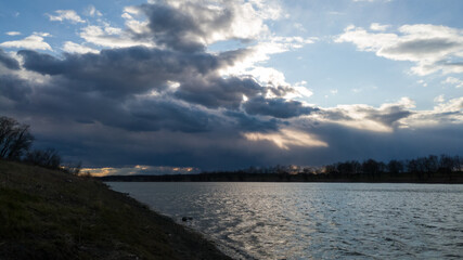 The sun’s rays break through the gloomy storm clouds above the river.