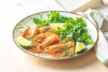 Beautiful boiled large shrimp in light ceramic plate with parsley and lime on pink concrete table surface.