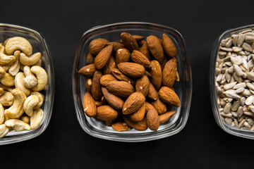 Almond, cashew and sunflower seeds in a small plates which standing on a black table. Nuts is a healthy vegetarian protein and nutritious food.