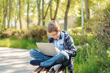 Obraz premium A teenager with a laptop on a park bench. Distance learning. Learn anywhere.