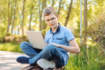 Obraz premium A teenager with a laptop on a park bench. Distance learning. Learn anywhere.