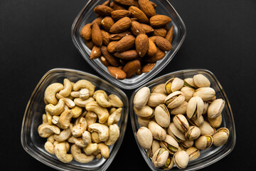 Almond, pistachio and cashew in a small plates which standing on a black table. Nuts is a healthy vegetarian protein and nutritious food.