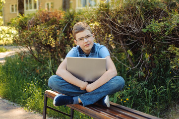 Fototapeta premium A teenager with a laptop on a park bench. Distance learning. Learn anywhere.
