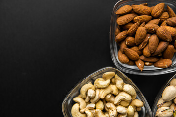 Almond, pistachio and cashew in a small plates which standing on a black table. Nuts is a healthy vegetarian protein and nutritious food.