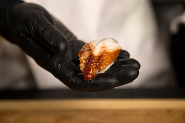 Chef hold in hand traditional sushi nigiri with eel, rice and nori. Close up of chef’s hand in black gloves near wooden board. Japanese food in restaurant. Cooking process of Asian dish preparation