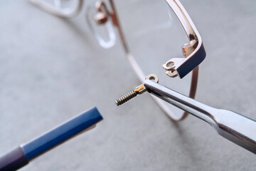 Closeup of setting new temple to broken eyeglasses by optician technician using professional tool in optician workshop. Professional repair and fixing damaged glasses in clinic office. Eyewear concept