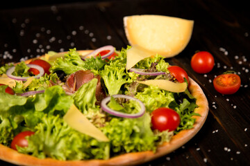 Traditional Italian pizza with jamon, Parmesan cheese, black olives, red onion and cherry tomatoes on wooden background with sea salt. Ingredients near Tasty uncut pizza.  Mediterranean rustic food
