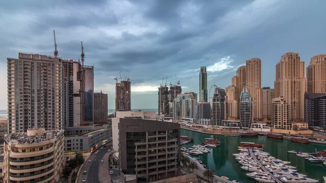 Towers and skyscrapers with Luxury yachts parked on the pier in Dubai Marina bay with city aerial view timelapse. Rainy clouds and lightnings. Early morning after sunrise