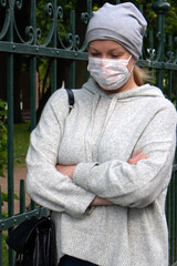 Woman in medical face mask dressed in grey with arms folded crosswise walking on the street