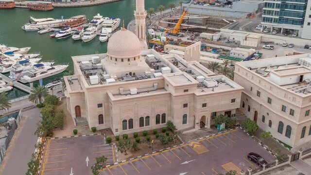 Yachts in Dubai Marina flanked by the Al Rahim Mosque with car parking and residential towers aerial night to day transition timelapse. Modern high rise skyline with boats and wooden dhows