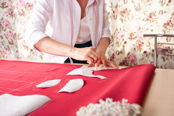 A beautiful seamstress woman in her own atelier makes a pattern on the red fabric. The master is painting the fabric for future clothing. A girl does things with her own hands.