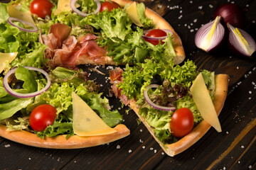 Fototapeta na wymiar Traditional Italian pizza with jamon, Parmesan cheese, black olives and cherry tomatoes on wooden background with sea salt. Ingredients near Tasty slice of pizza. Mediterranean rustic food 