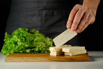 Diced tofu cheese in the hands of cooks on a wooden board. High quality photo