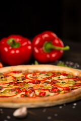Side view of pizza with bell pepper, green olives, smoked sausages, mozzarella cheese, pepperoni, salami, chili pepper, champignons on wooden board with two bell peppers on background. uncut pizza
