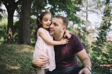 Portrait of daughter hugging her father in park. Bearded man and cute little girl hugging in nature.