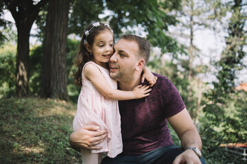 Fototapeta premium Portrait of daughter hugging her father in park. Bearded man and cute little girl hugging in nature.