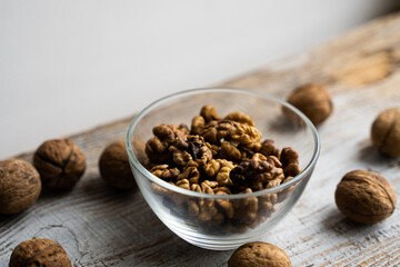 Walnut in a smale plate with scattered shelled nuts and whole nut which standing on a wooden vintage table. Walnuts is a healthy vegetarian protein nutritious food. Walnut on rustic old wood.