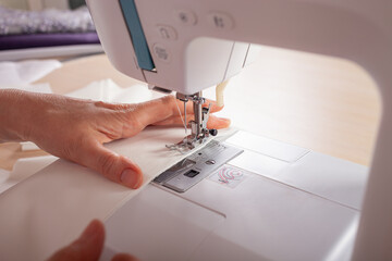 The seamstresses are stale on the sewing machine details of clothing made of fabric. The master sews new clothes on the sewing machine. A woman makes wardrobe details with her own hands. Business