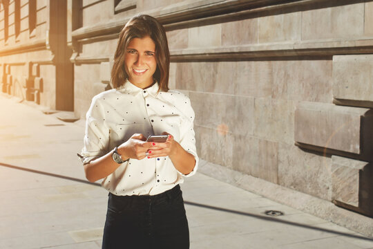 Young fancy girl using her smart phone while strolling in the city in sunny afternoon, attractive brunette female using cellular phone with copy space area for your text message or promotional content