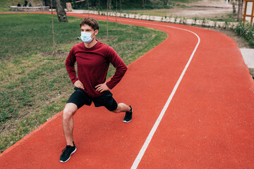 Obraz premium Sportsman in medical mask doing lunges while working out on running path in park