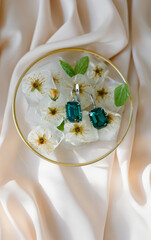 
Ice cubes with flowers and emerald earrings on silk. Fashion photography accessories. The concept of jewelry.
