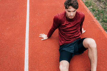 High angle view of handsome sportsman sitting on running track in park