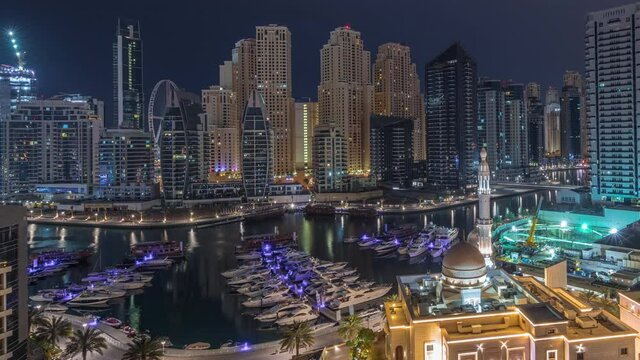 Yachts in Dubai Marina flanked by the Al Rahim Mosque and residential towers and skyscrapers aerial night to day transition timelapse. Modern high rise skyline with boats and wooden dhows