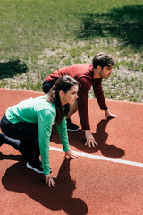 Side view of couple in sportswear standing in starting position on track in park