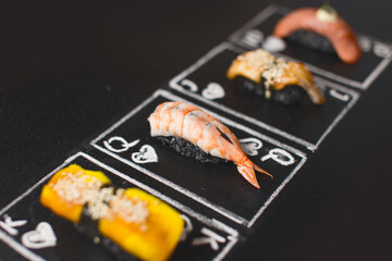 Hand drawn Poker cards, Japanese sushi nigiri with black rice and shrimp in focus on chalkboard. Near Asian food with salmon tataki, eel and Japanese omelette. Ebi nigiri between Unagi and Tomago